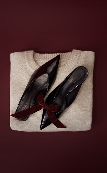 A pair of black pointed mules on top of a folded beige sweater.