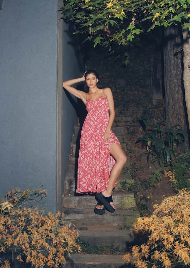 Une mannequin porte une robe maxi rose imprimée avec une fente sur la jambe. 