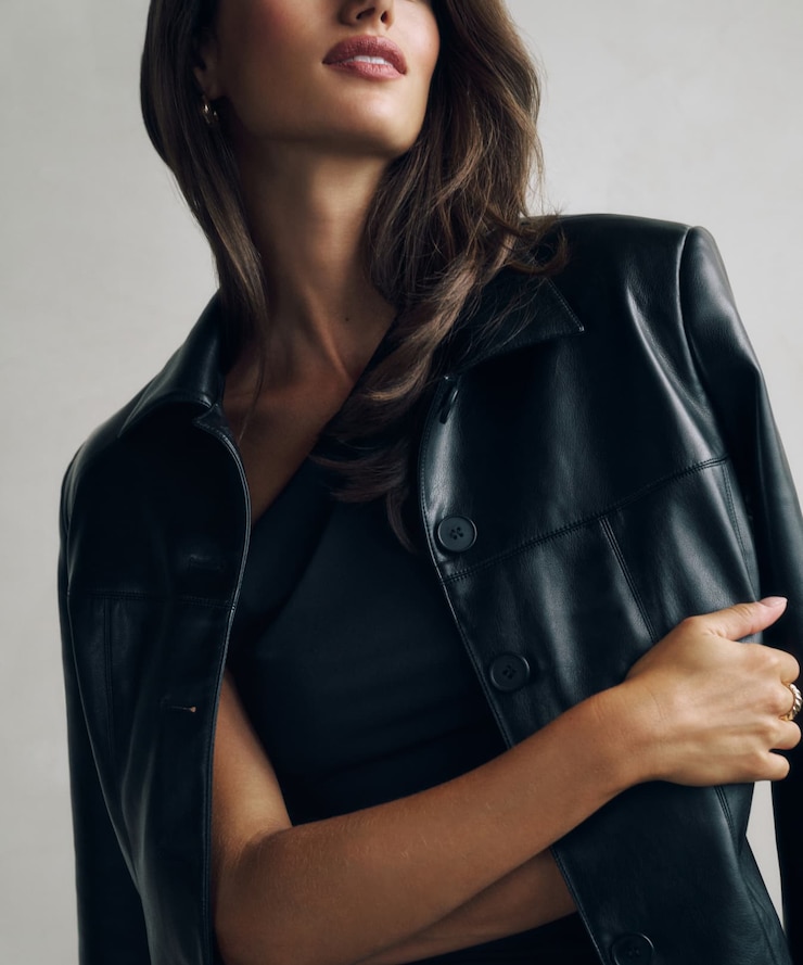 Model is wearing a black faux leather jacket over a black top.