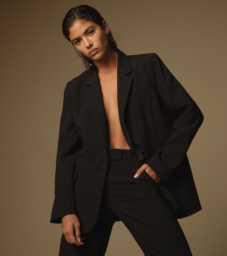 Une mannequin porte un veston noir ouvert avec un pantalon noir assorti.