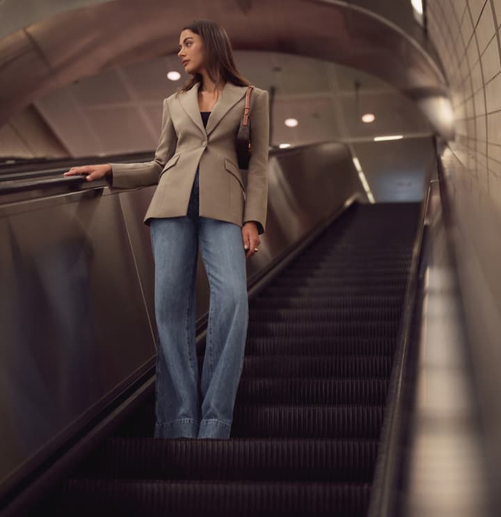 La mannequin porte un veston cintré brun avec un jean bleu pâle.