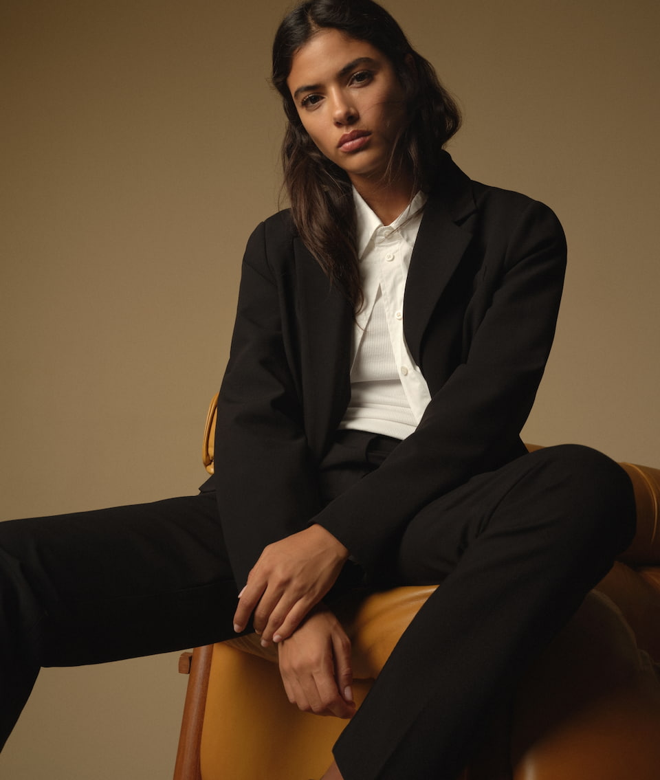 Une mannequin porte une chemise boutonnée blanche avec un veston noir et un pantalon noir assorti.