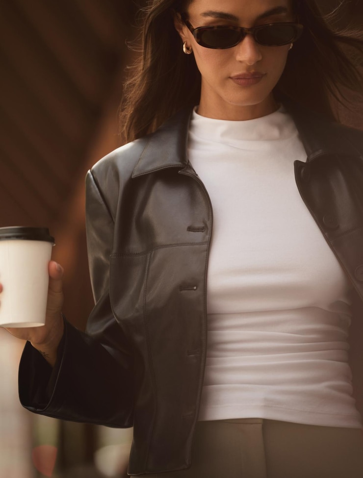 Model is wearing a black faux leather jacket over a white shirred tank top.