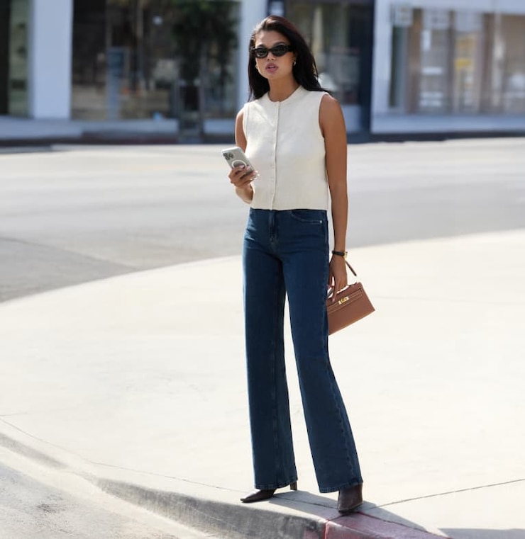 Model is wearing a white sleeveless cardigan with black wide leg jeans.