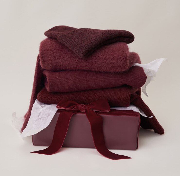 A folded pile of burgundy knitwear including a beanie, a cardigan, and a sweater.