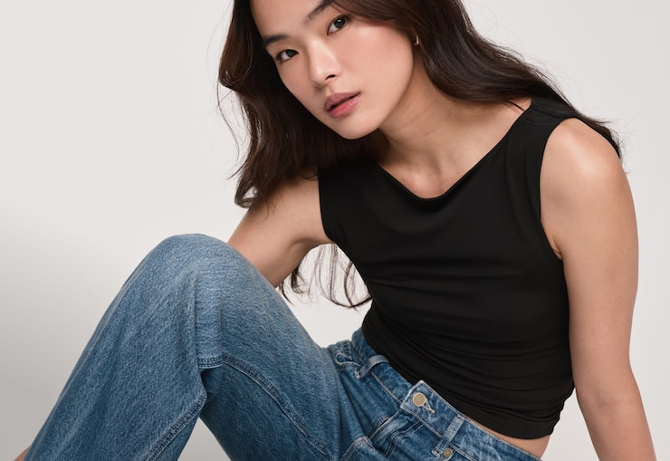 Model is wearing a black tank top and blue straight leg jeans..