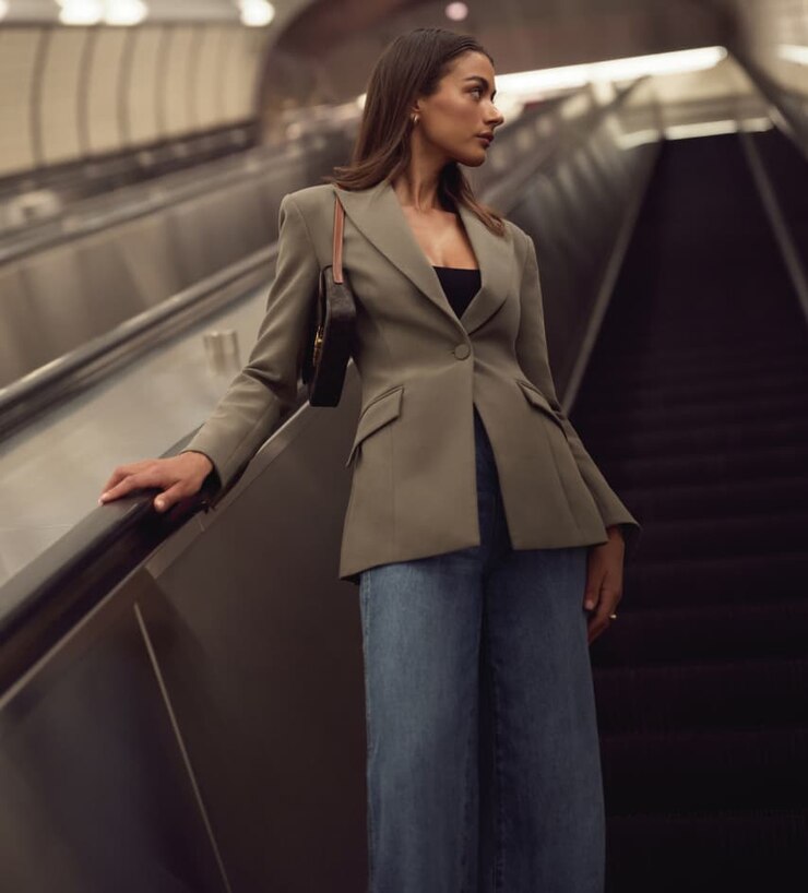 Model is wearing a brown cinched blazer and blue wide leg jeans.