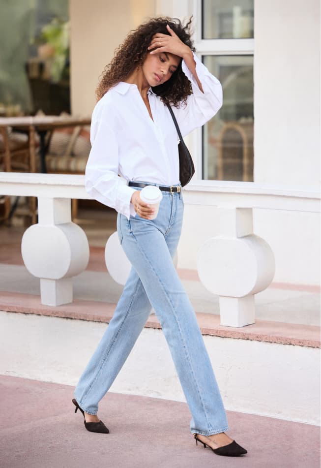 Model is wearing a white button up shirt with light blue straight leg jeans and a black leather belt.