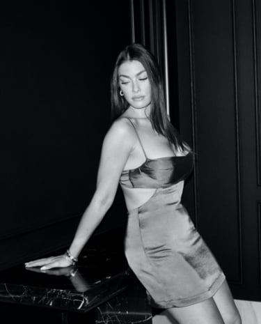 Katherine sitting on table in satin cut out mini dress.
