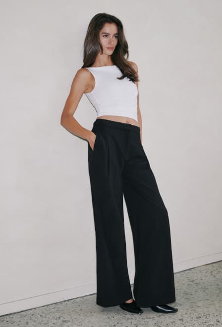 Model is wearing a white boat neck tank top and black wide leg pants.