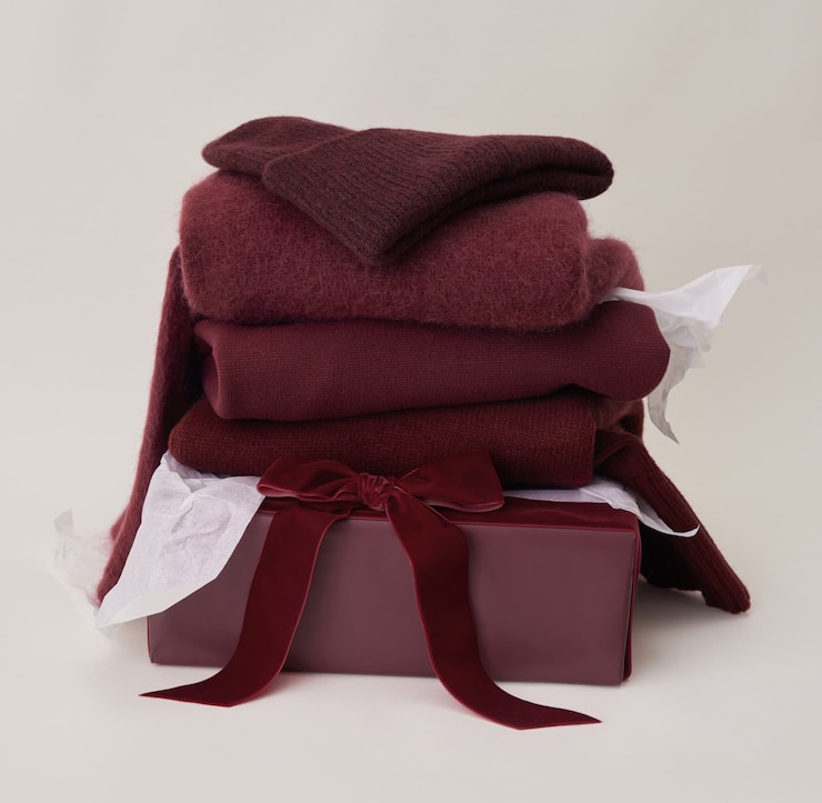 A folded pile of burgundy knitwear including a beanie, a cardigan, and a sweater.