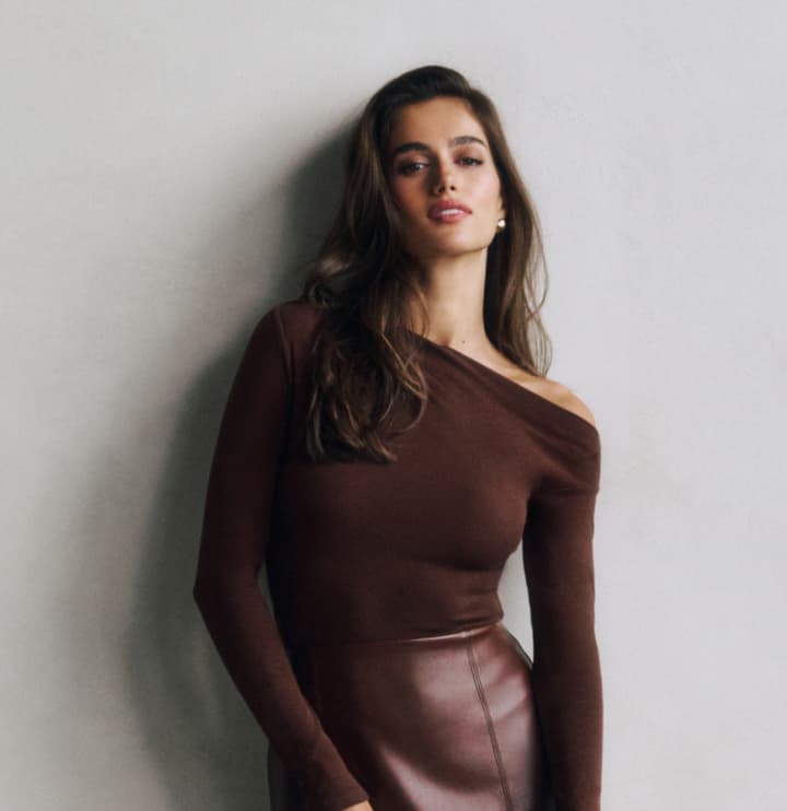 Model is wearing a brown off shoulder top and a brown faux leather mini skirt.
