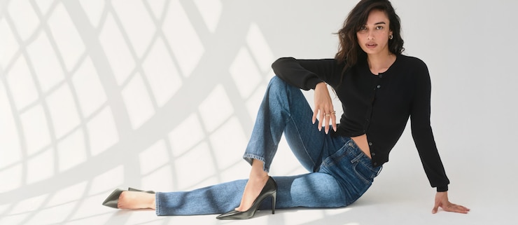 Model is wearing a black cardigan and blue slim leg jeans.