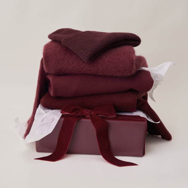 A folded pile of burgundy knitwear including a beanie, a cardigan, and a sweater.