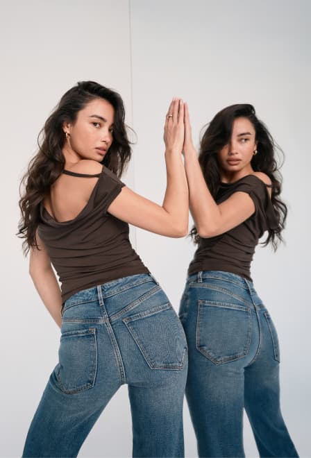 Model is wearing a brown open back top and medium wash jeans.
